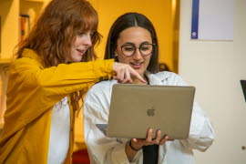Ett par studenter som står och kollar på en laptop, ena studenten pekar på skärmen.