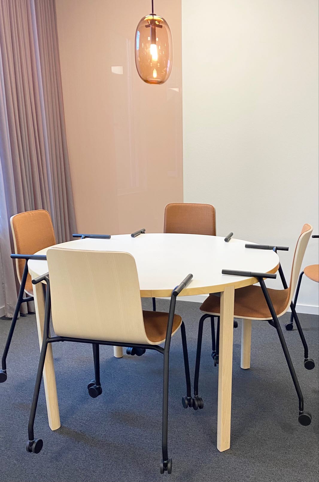 Table with four chairs. Above the table hangs an orange lamp in a drop shape.