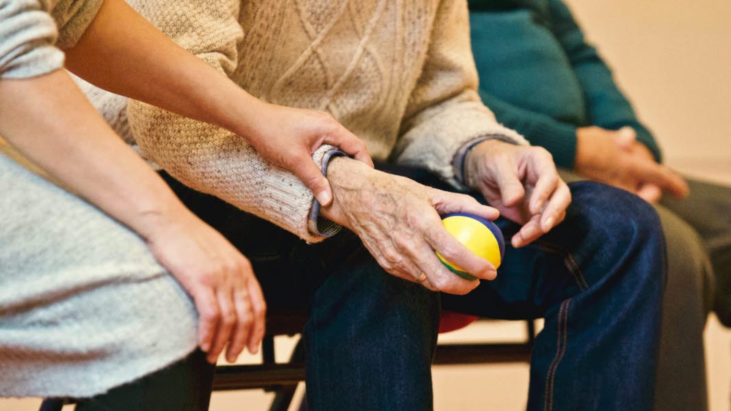 Äldre person håller i en stressboll, en annan person sitter bredvid.