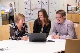 Tre medarbetare vid ett konferensbord diskuterar framför en dator