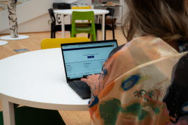 En kvinna sitter vid ett runt bord med en bärbar dator framför sig.