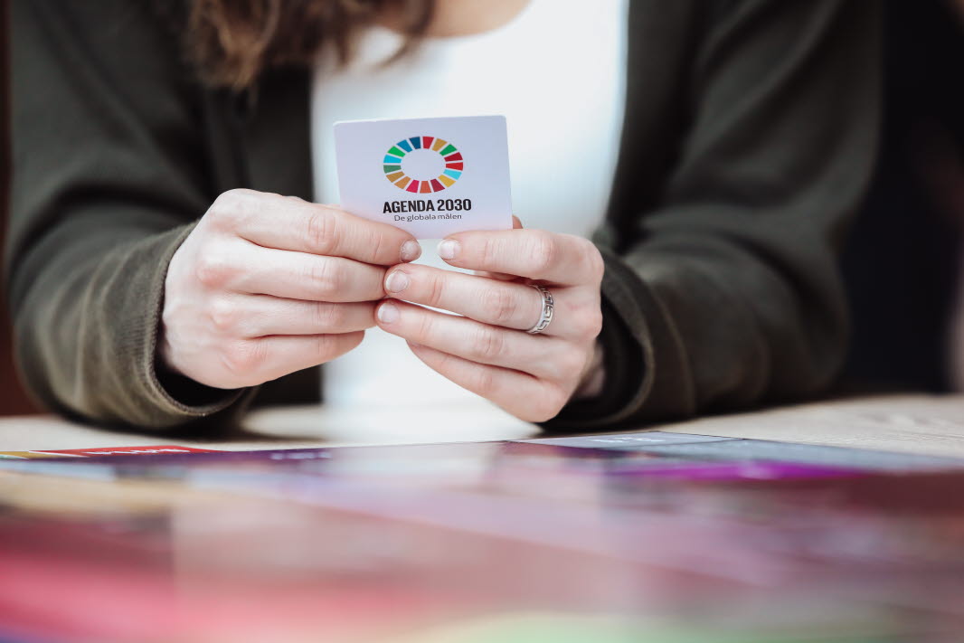 Närbild av två händer håller i ett kort med texten "Agenda 2030 - det globala målen"