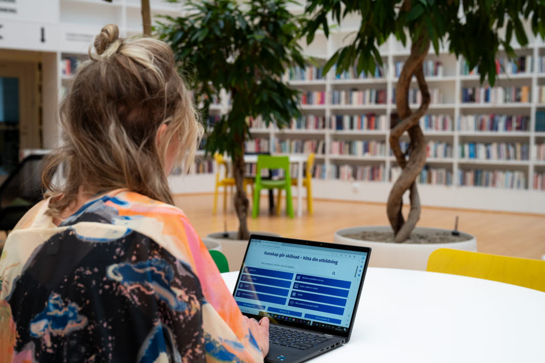 En kvinna sitter vid ett runt bord med en bärbar dator framför sig i högskolans bibliotek