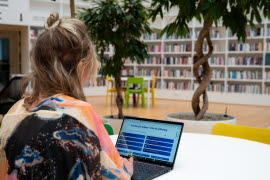 En kvinna sitter vid ett runt bord med en bärbar dator framför sig i högskolans bibliotek