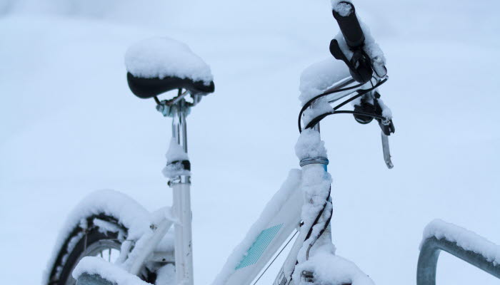 En cykel i ett cykelställ. Cykeln har mycket snö på sig. 