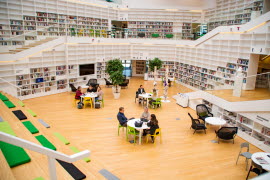 Studenter som sitter i ett bibliotek och studerar vid sina laptops samtidigt som de samtalar.