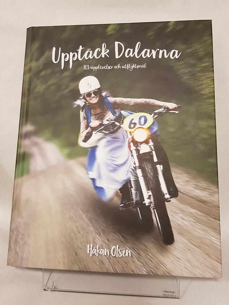 Bok med bild på person med klänning som kör en motorcykel. Texten "Upptäck Dalarna" i vitt.