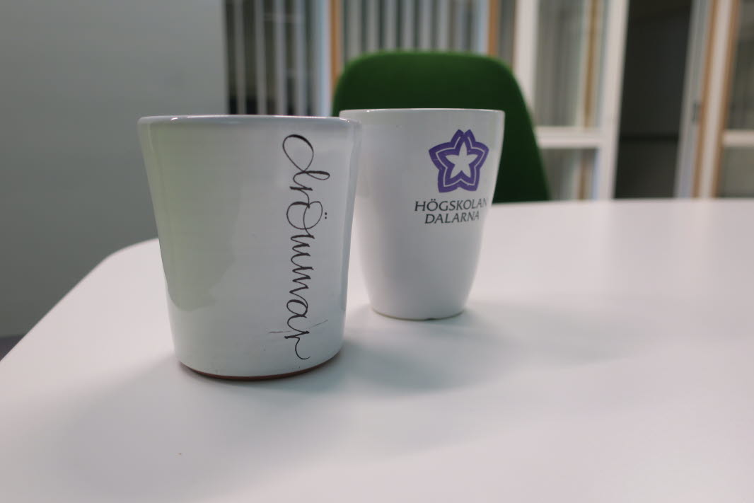 Närbild på två kaffekoppar på ett vitt bord, en med texten drömmar och en med Högskolan Dalarnas logotyp