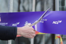 En hand håller i en sax och klipper av ett lila band.