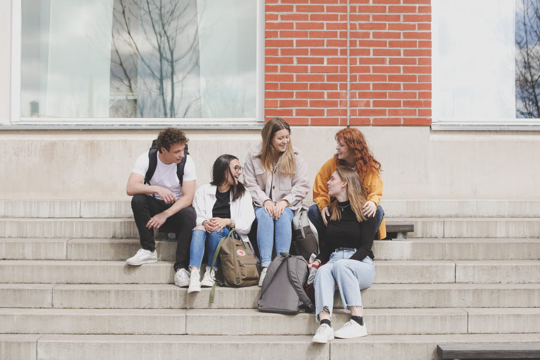 En grupp studenter sitter på en trappa och pratar