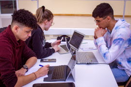 En grupp studenter som sitter vid ett bord med sina laptops och studerar.