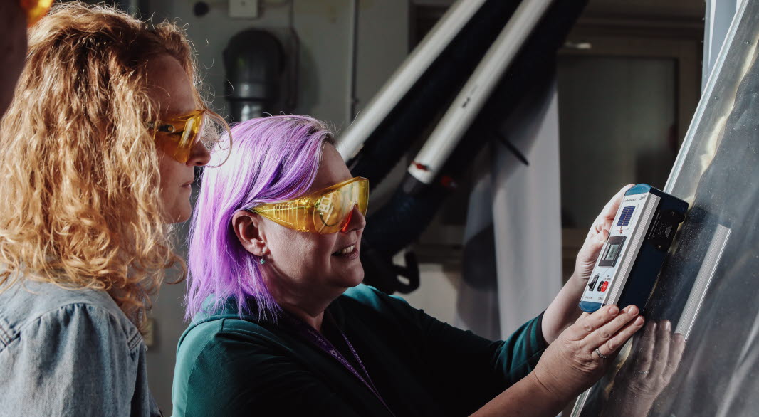 Two persons with protective glasses stand indoors in front of measuring panel laboratory for solar simulation