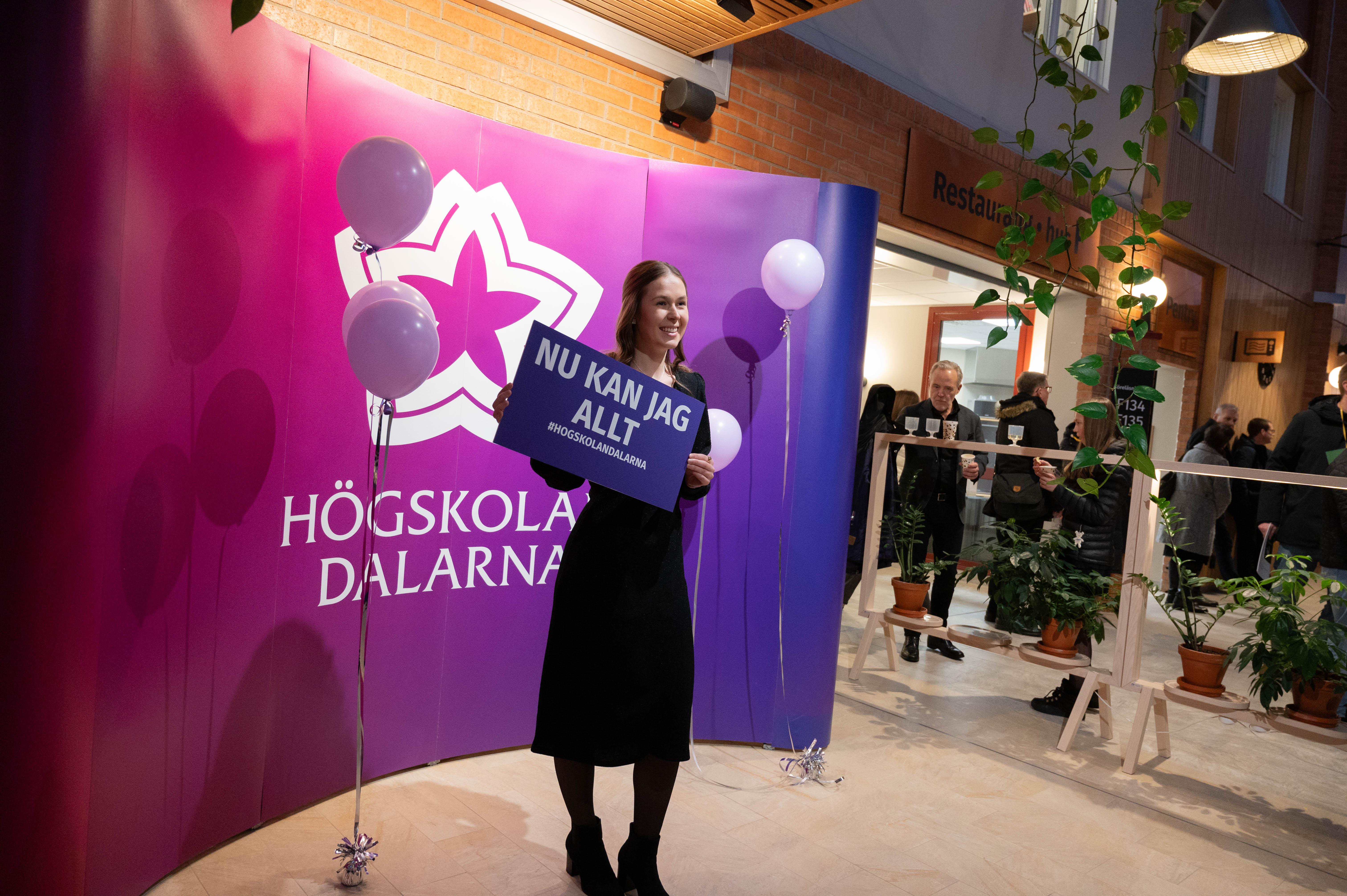 A person holding a sign, standing in front of a wall with Dalarna University logo.