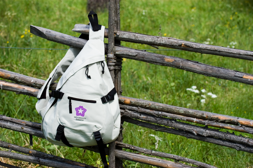 En ryggsäck med Högskolan Dalarna logotyp hängandes på en gärdesgård.