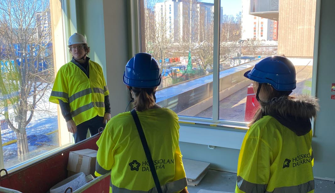 Tre personer i gula västar och bygghjälm i ett rum på nya Campus Borlänge.