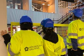 Tre personer i gula västar och bygghjälm tittar ut på byggandet av kunskapstrappan på nya Campus Borlänge.