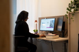 Person med mörka kläder och mörkt hår sitter framför dator. 